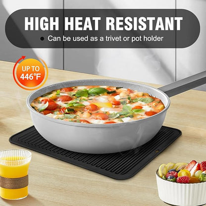 Frying pan with food on a heat-resistant mat, surrounded by a glass of juice and a bowl of fruit.