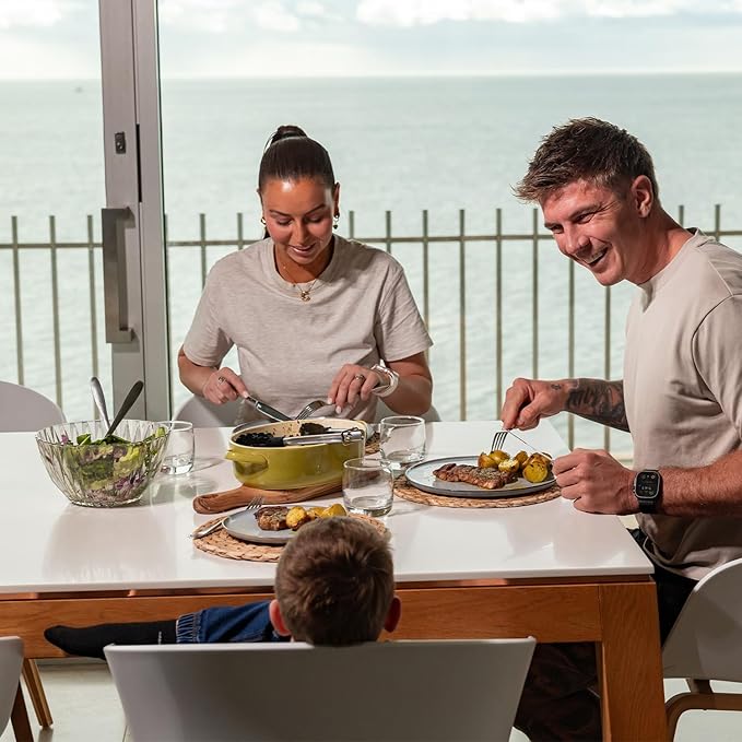 Family of three enjoying a meal together at a table with a view of the ocean.