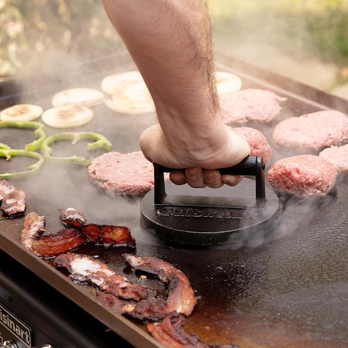 Person using a burger press on a grill with burgers and bacon cooking.