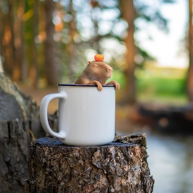 Small figurine of a rodent on top of a white mug with a blurred natural background